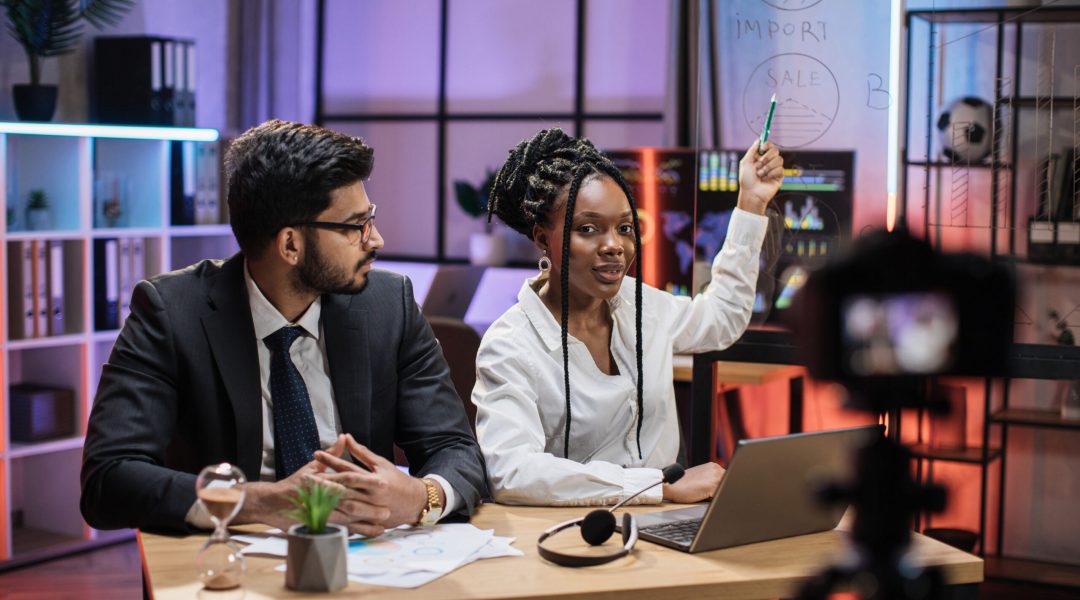 Attractive male and female financiers, arab manager and confident african american business woman explaining online economic charts on glass board to their colleagues sitting in front of video camera.